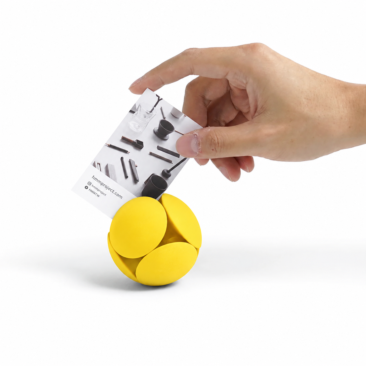 HMM Eraser Ball in Sunshine Yellow als Kartenhalter – eine Hand steckt eine Visitenkarte zwischen die gelben Radiergummi-Elemente.