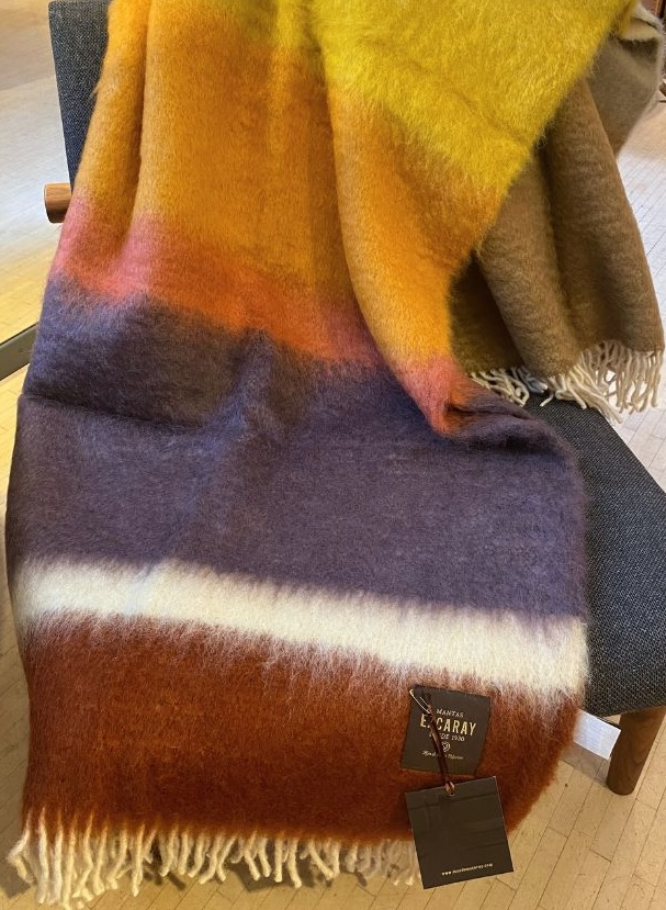MANTAS EZCARAY Matisse M-61 Mohair-Wolldecke mit breiten Streifen in Gelb, Orange, Bordeaux und Beige, cremeweissen Fransen, über einem Holzstuhl drapiert